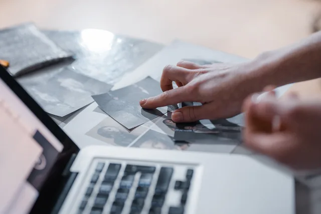 A hand arranges vintage photographs near a laptop in a modern workspace. Bereits verwendete Bilder im Archiv erkennen