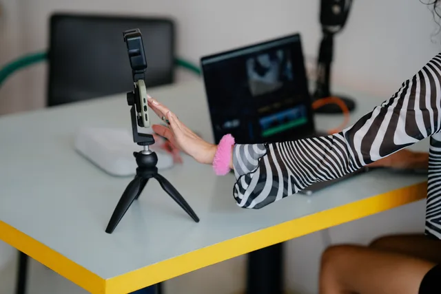 Woman adjusting smartphone on tripod with laptop setup for video editing. Creator-Tool-Kosten