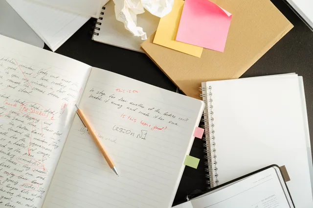 A cluttered desk with notebooks, sticky notes, and stationery for educational purposes. Fakten und Zitate nach einer KI-Überarbeitung prüfen