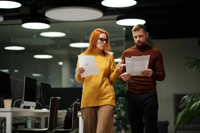 Two colleagues review documents while walking through a contemporary office space. Feedback an der richtigen Dateiversion sammeln