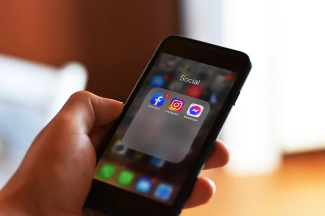 Close-up of hand holding smartphone showing social media apps like Facebook and Instagram. Planungsfunktionen nach unterstützten Plattformen prüfen