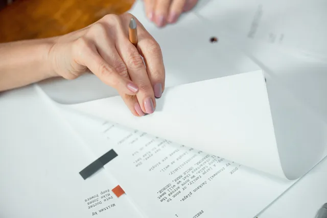 Close-up image of hands turning pages of a document on a desk indoors. Transkriptfehler vor der Weiterverwendung korrigieren